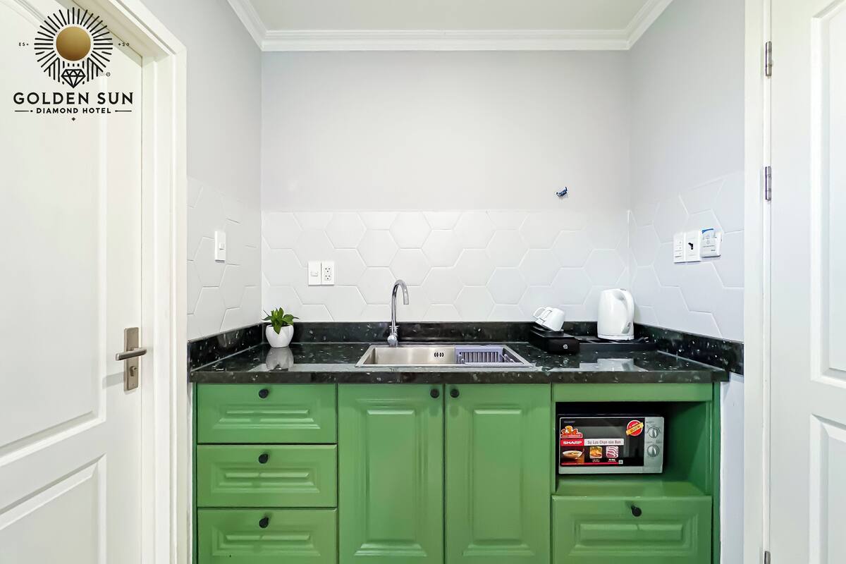 A kitchen with green cabinets, a black countertop, a sink, and a coffee machine.