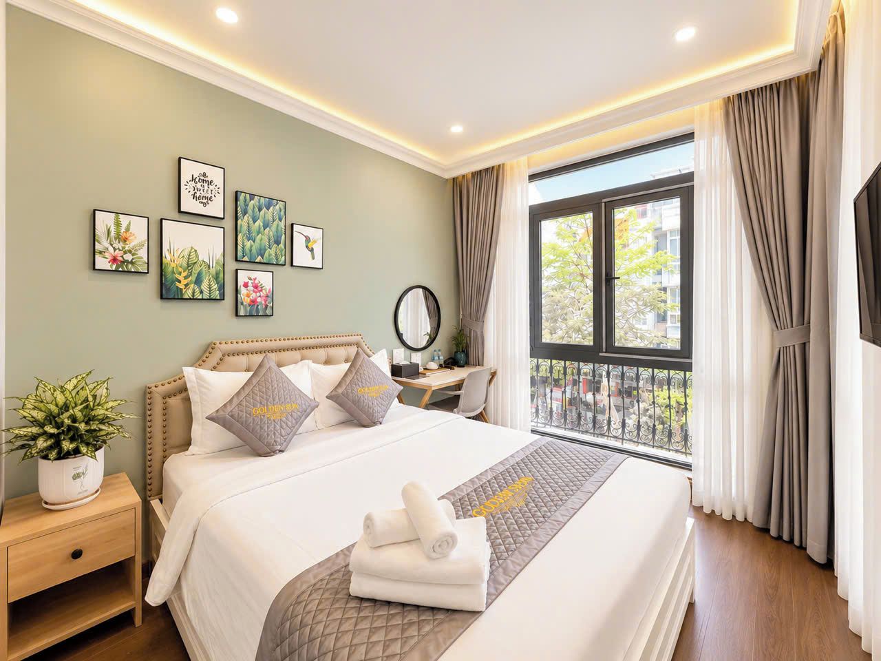 Ein Hotelzimmer mit Bett, Nachttisch, Topfpflanze, Wandbild und Blick aus dem Fenster.