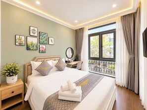 A hotel room with a bed, bedside table, potted plant, artwork on the wall, and a view through the window.