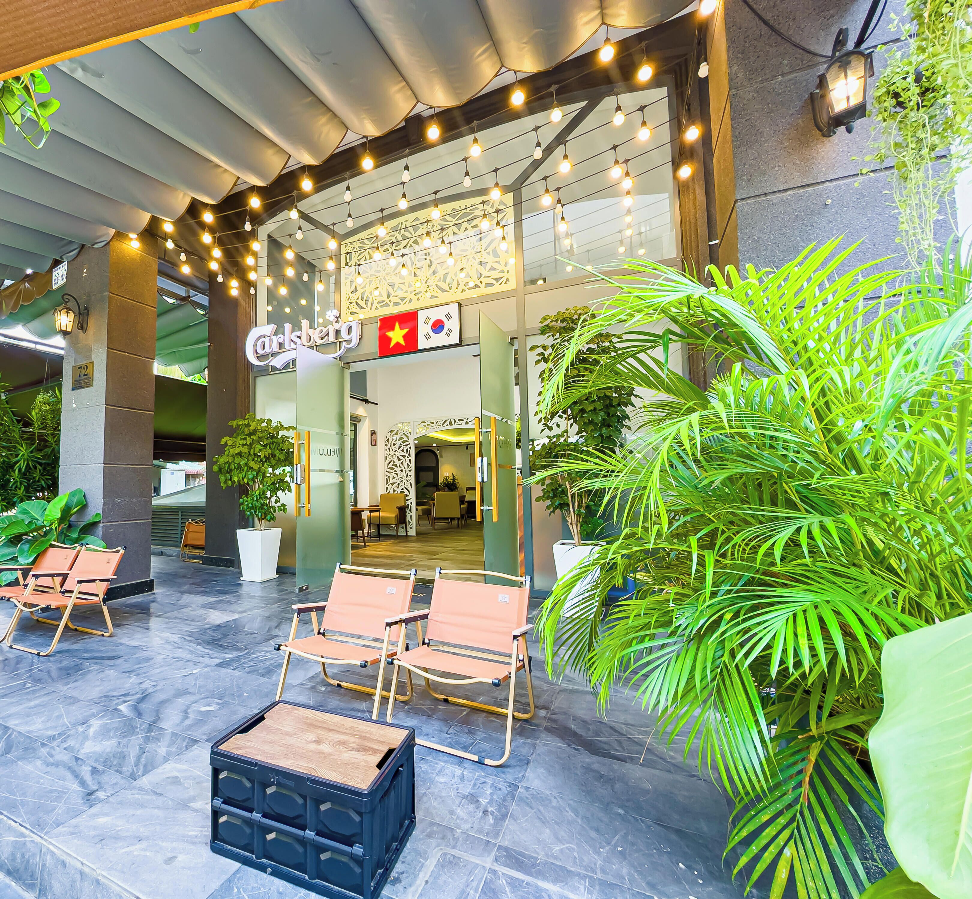 An outdoor seating area with chairs and a table, a sign for 'Carlsberg,' and potted plants.