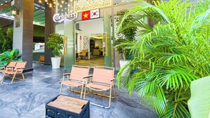 An outdoor seating area with chairs and a table, a sign for 'Carlsberg,' and potted plants. - Golden Sun Hotel Apartments (Ho Chi Minh City)