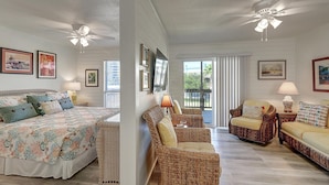 A bedroom with a bed, a nightstand, and a window. There is a living area with a sofa, a chair, and a lamp. The room has white walls and a ceiling fan. - Secluded, yet close to everything Port A has to offer. Sit on the deck and watch (Port Aransas)