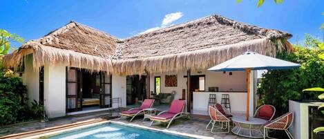 A poolside area with a thatched-roof structure, lounge chairs, and a small table.