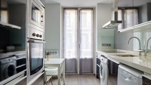 A modern kitchen with stainless steel appliances, a white countertop, and a window with sheer curtains. - Gros Arena I | The Rentals Collection (San Sebastián)