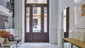 A hotel entrance with a dark brown door, a small table with a vase of flowers, and a bench. - Gros Arena I | The Rentals Collection (San Sebastián)