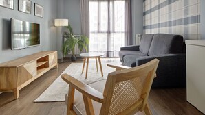 A modern living room with a grey sofa, wooden coffee table, and a TV on the wall. - Gros Arena II | The Rentals Collection (San Sebastián)