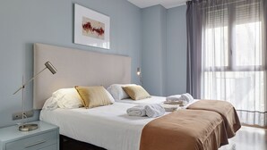 A modern bedroom with a bed, bedside tables, and a large window with curtains. - Gros Arena II | The Rentals Collection (San Sebastián)