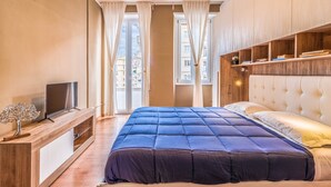 Un dormitorio con una cama grande, un televisor sobre un mueble de madera y vistas a la ciudad por la ventana.