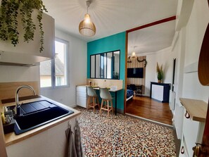 A compact kitchen with a sink, a dining area with chairs, a teal accent wall, and a patterned floor. - THE COCON (Rennes)