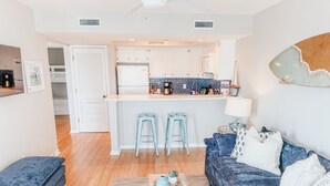 Un espacio habitable compacto con kitchenette, un sofá, una mesita de centro y un taburete pequeño.