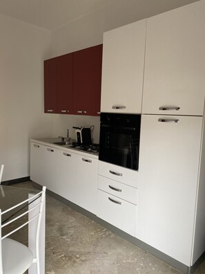 Cozinha com armários brancos, forno preto e um armário superior vermelho.