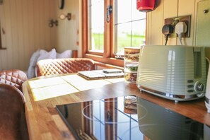 Une table en bois, un appareil électroménager vert, une fenêtre donnant sur un paysage et une lampe rouge.
