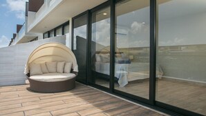 Un espace extérieur moderne, aménagé avec des sièges, comprenant un fauteuil rond et rembourré, ainsi qu’un balcon fermé par des parois de verre.