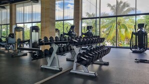 Une salle de sport équipée de matériel de musculation, dotée de grandes fenêtres et offrant une vue sur des palmiers.