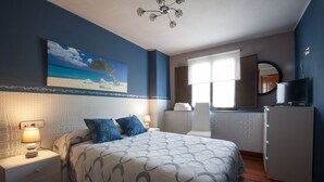 Een slaapkamer met een bed, nachtkastjes, een dressoir, een televisie en een schilderij van een strandgezicht.