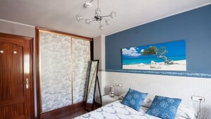 Een slaapkamer met een bed, een nachtkastje, een schilderij van een strand en een kledingkast.