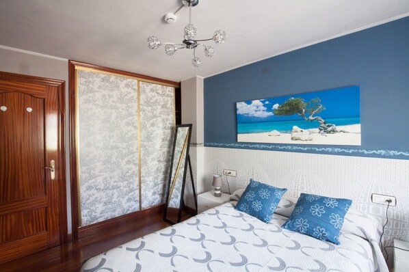 Un dormitorio con una cama, una mesita de noche, un cuadro de una escena de playa y un armario.