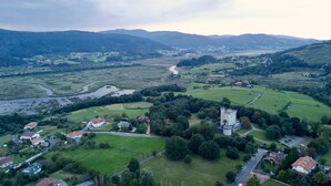 Een luchtbeeld van een landelijk gebied met een opvallende, kasteelachtige constructie, omringd door groene velden en verspreide huizen.