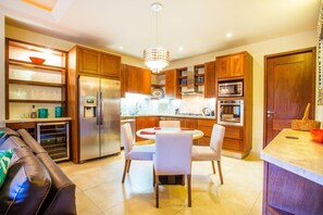 Een moderne keuken met houten kastjes, roestvrijstalen apparatuur en een eethoek met een ronde tafel en stoelen.