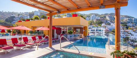 A rooftop pool area with lounge chairs and umbrellas, a bar, and a view of the cityscape.