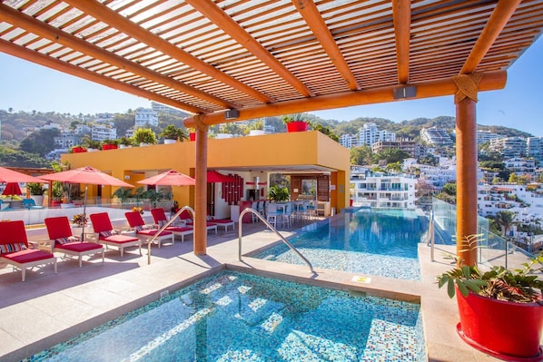 A rooftop pool area with lounge chairs and umbrellas, a bar, and a view of the cityscape. - Serene 1BR w/ Patio & Workspace (Puerto Vallarta)