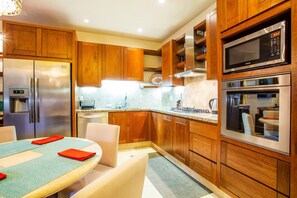 A modern kitchen with wooden cabinets, stainless steel appliances, and a dining area with a table and chairs. - Serene 1BR w/ Patio & Workspace (Puerto Vallarta)