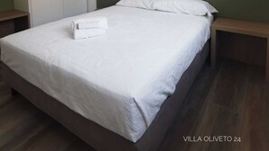 Un lit bien fait, avec du linge de lit blanc, une tête de lit verte et deux tables de chevet surmontées de lampes noires. Une œuvre d’art encadrée est accrochée au mur, au-dessus du lit.