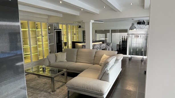 Una sala de estar moderna con un sofá seccional color beige, una mesa de centro de vidrio y una unidad de almacenamiento empotrada con estantes iluminados.