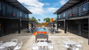 An outdoor pool area with lounge chairs and tables, a foosball table, and a view of the ocean. - Boxo Diani (Diani Beach)