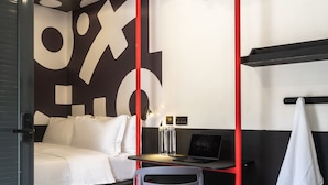 A hotel room with a bed, a desk with a laptop, a chair, and a towel hanging on the wall. - Boxo Diani (Diani Beach)