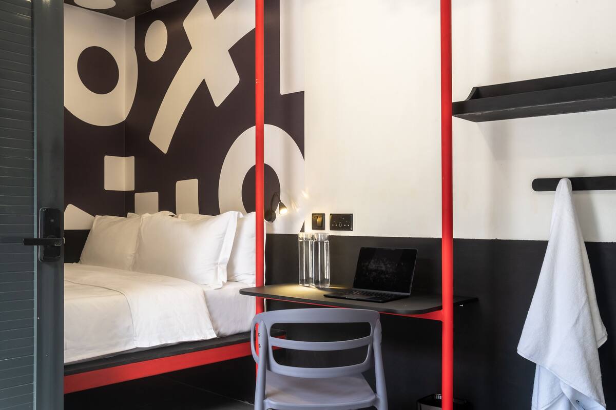 Habitación de hotel con una cama, un escritorio con una computadora portátil, una silla y una toalla colgada en la pared.