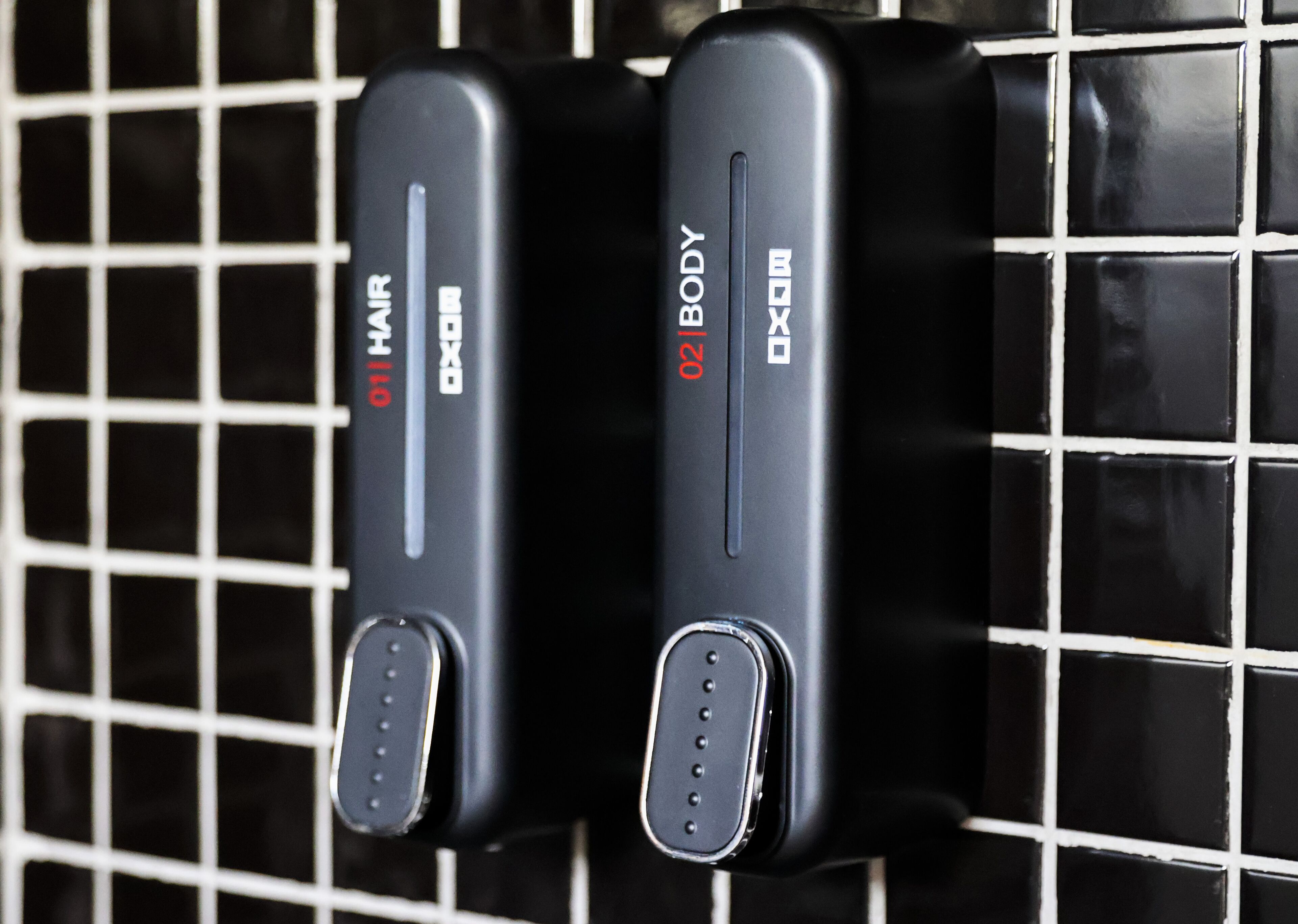 Two black hair dryers with labels "01 HAIR" and "02 BODY" mounted on a tiled wall.