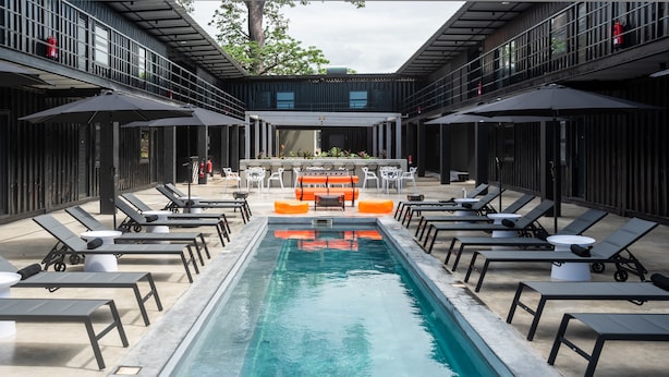 A modern outdoor pool area with lounge chairs and umbrellas, surrounded by a building with a balcony. - Boxo Diani (Diani Beach)