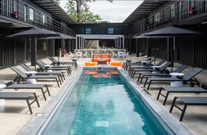 A modern outdoor pool area with lounge chairs and umbrellas, surrounded by a building with a balcony. - Boxo Diani (Diani Beach)