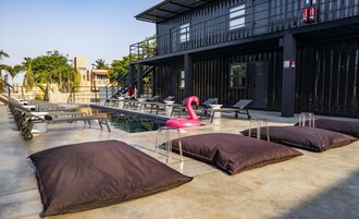 Un área de piscina con sillas de descanso, un flotador de flamenco y un edificio moderno con balcón.