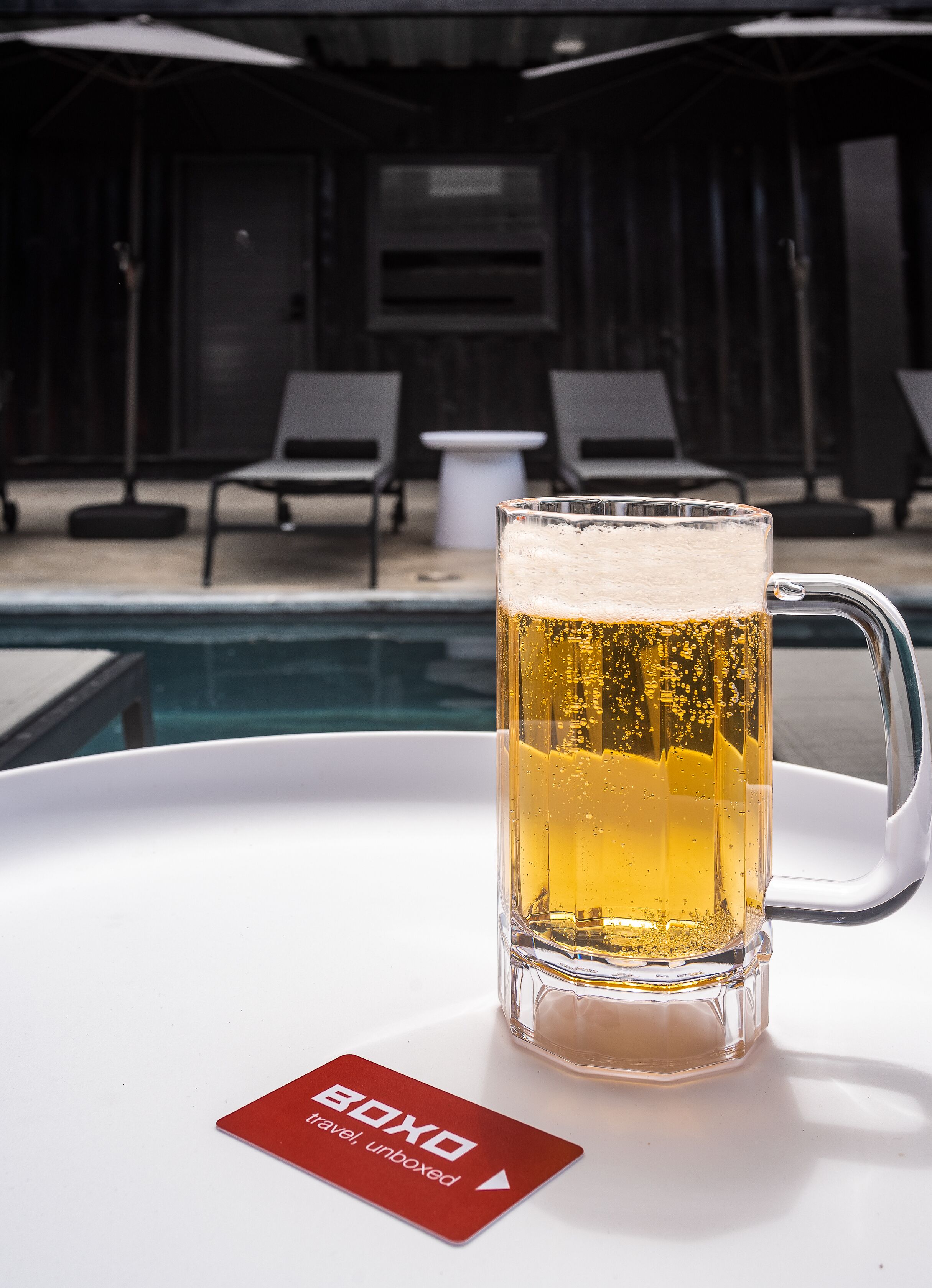 A glass of beer on a white tray with a red card beside it.