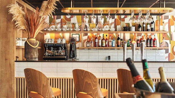 A bar area with wooden chairs, a coffee machine, and a variety of bottles and glasses on shelves. - Logis Hôtel Larivaut, Puy-Guillaume (Puy-Guillaume)