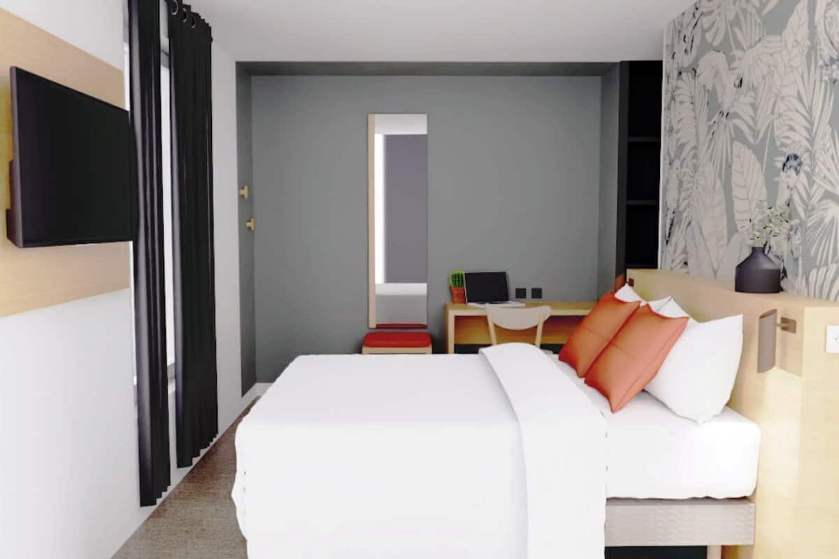 A hotel room with a bed, a desk, a chair, a television, and a door.