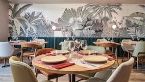 A restaurant with round tables, chairs, and a mural of tropical foliage on the wall. - Logis Hôtel Larivaut, Puy-Guillaume (Puy-Guillaume)