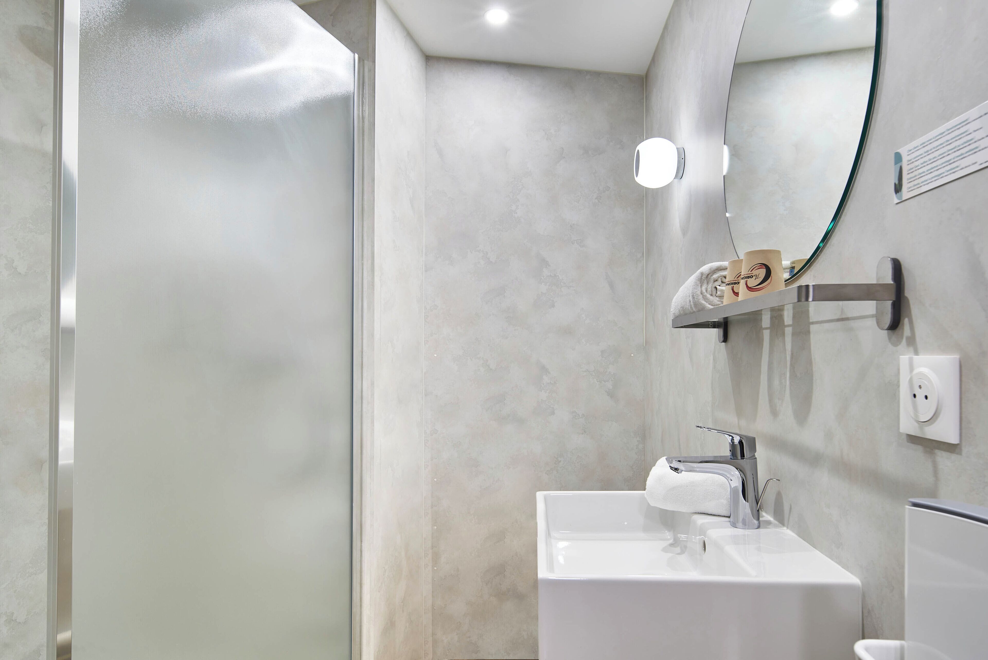 Une salle de bain moderne avec une douche à parois de verre, un lavabo blanc et un miroir doté d’un porte-serviettes.