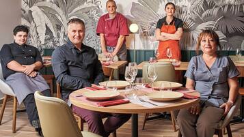 Un groupe de personnes est assis autour d’une table ronde, devant des assiettes, des couverts et des verres à vin.