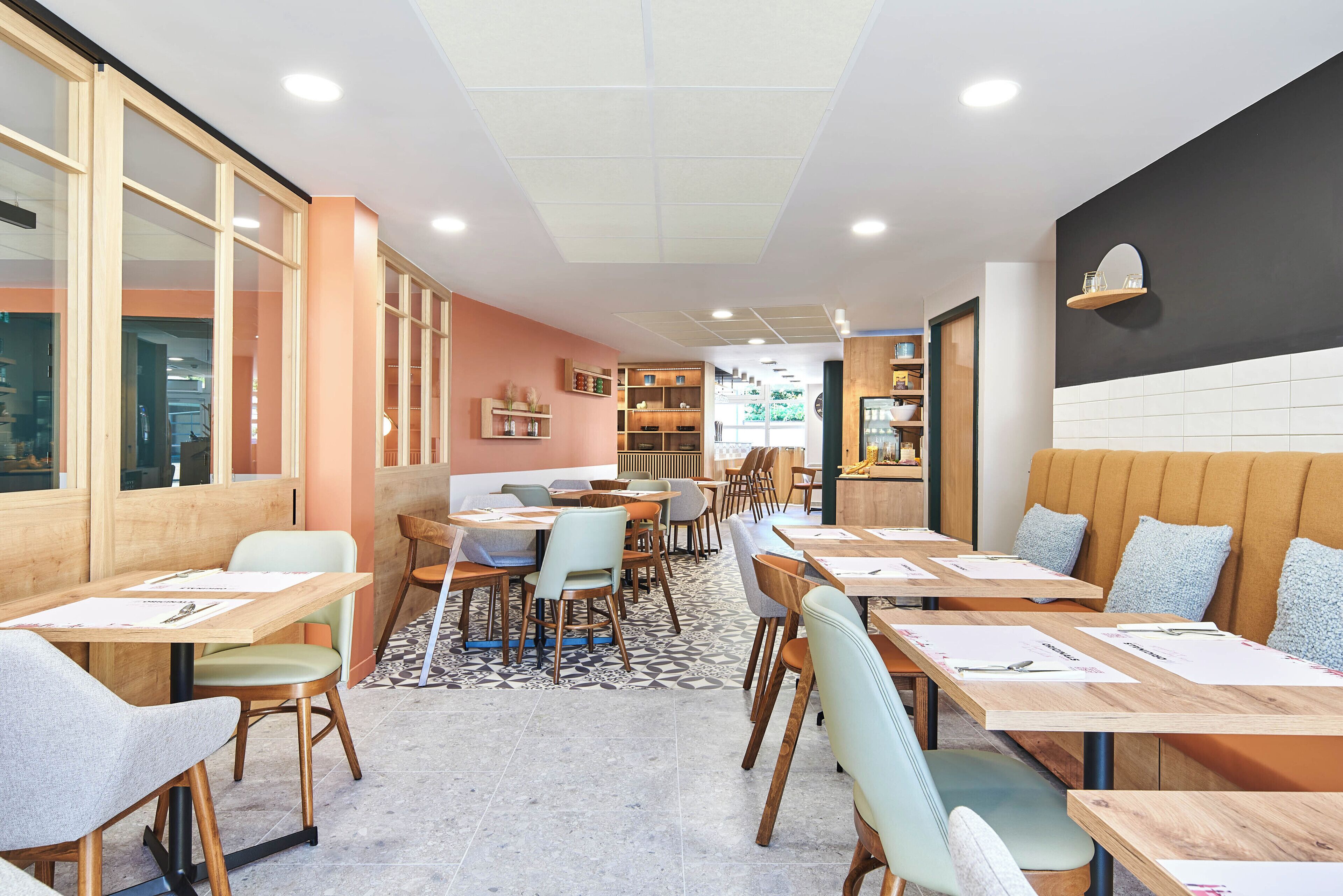 Un café moderno con mesas y sillas de madera, suelo estampado y pared con azulejos blanco y negro.