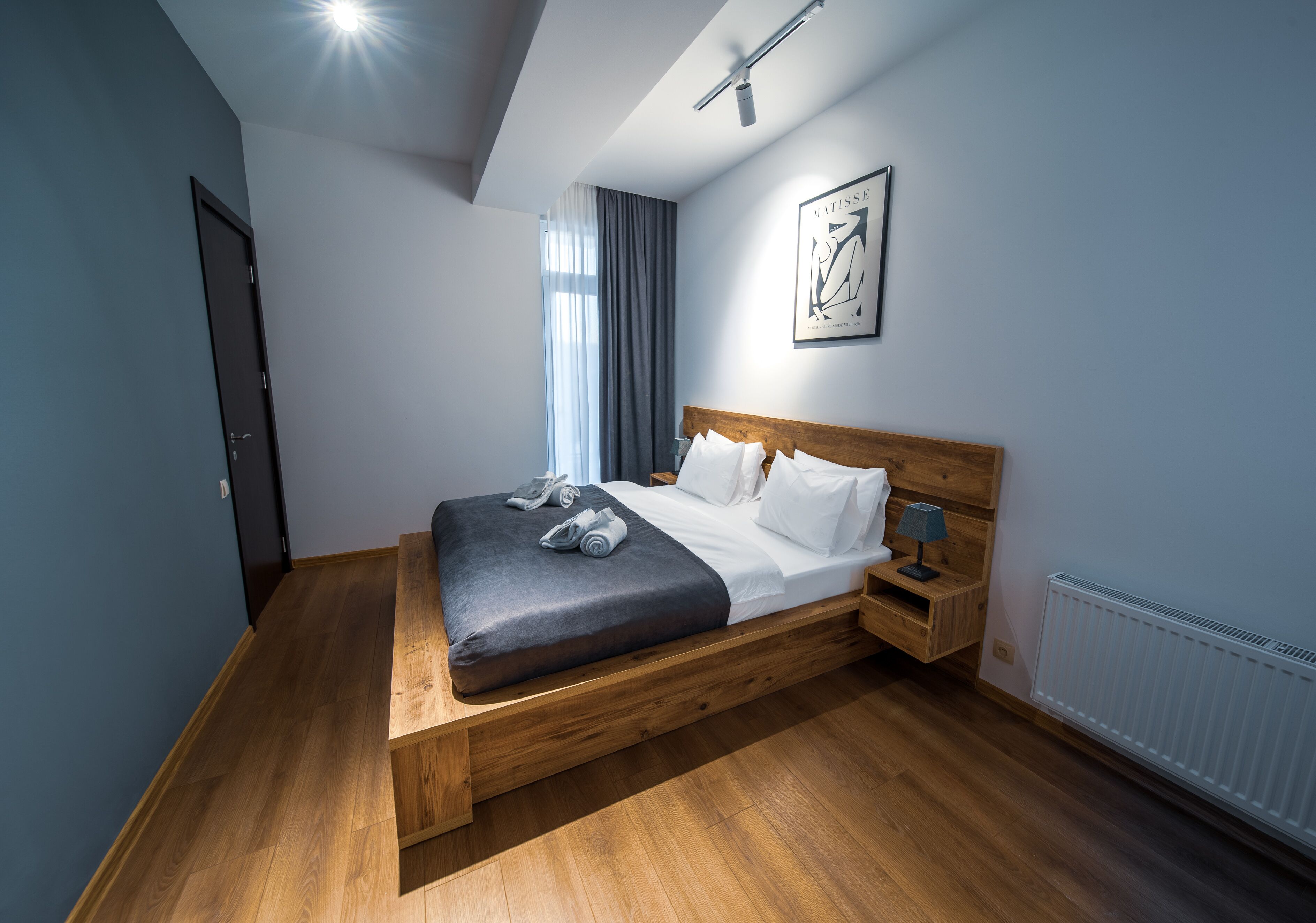 A modern bedroom with a wooden bed, a nightstand, a lamp, and a framed artwork on the wall.