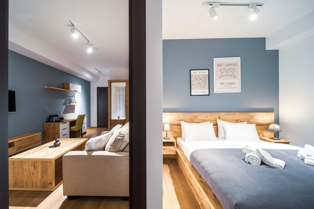A modern room with a wooden desk, a sofa, a bed, and artwork on the wall.