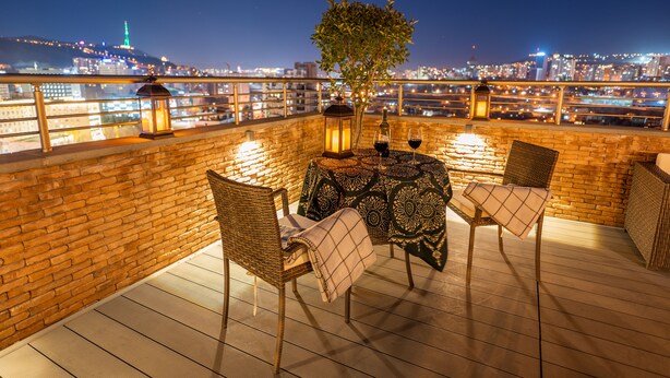 A rooftop terrace with wicker chairs, a table with a patterned tablecloth, and lanterns. A tree is in the center, and the city skyline is visible in the background. - Reed Hotel Tbilisi (Tbilisi)