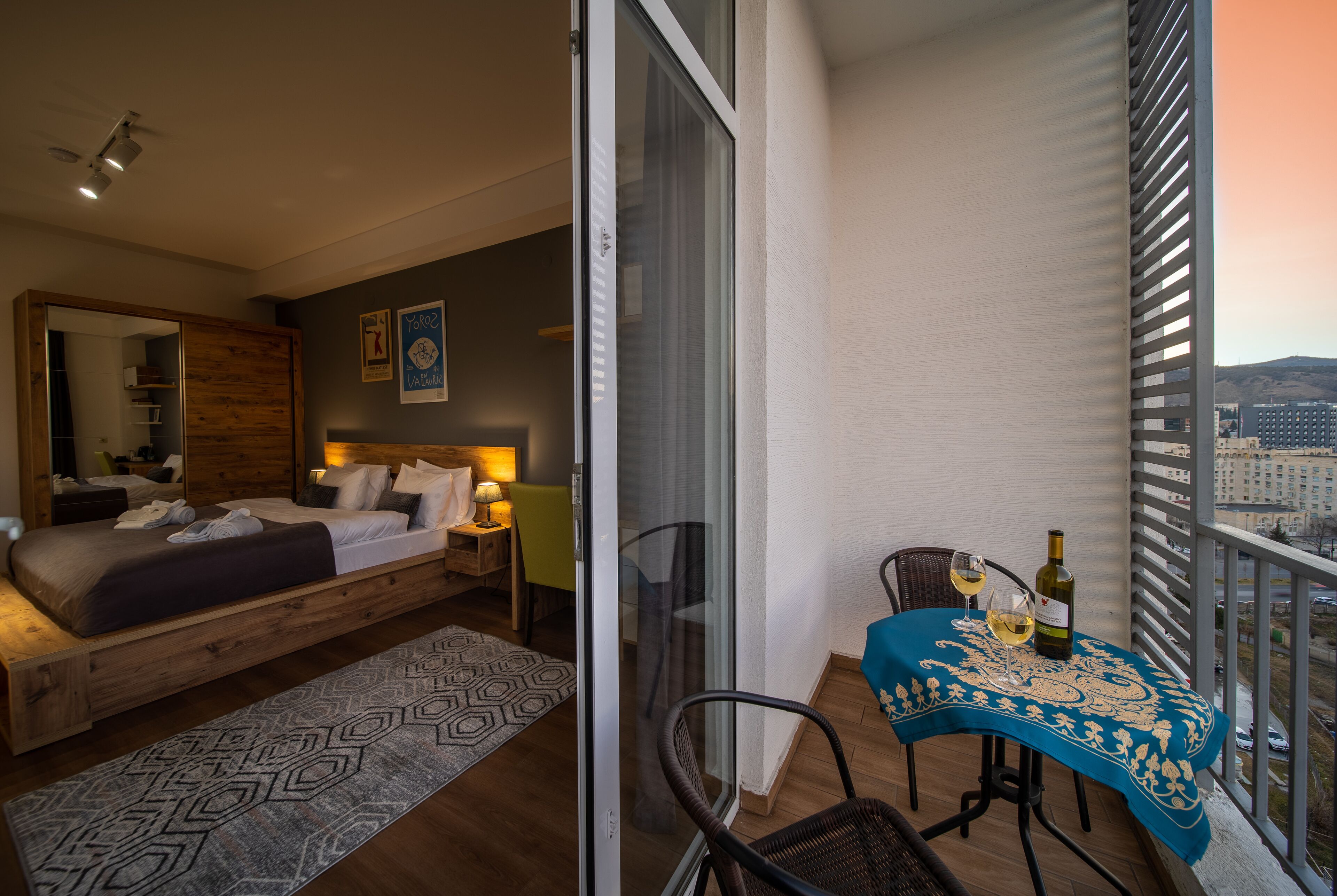 Une chambre à coucher avec un lit, une table de chevet et une vue sur la ville depuis un balcon.