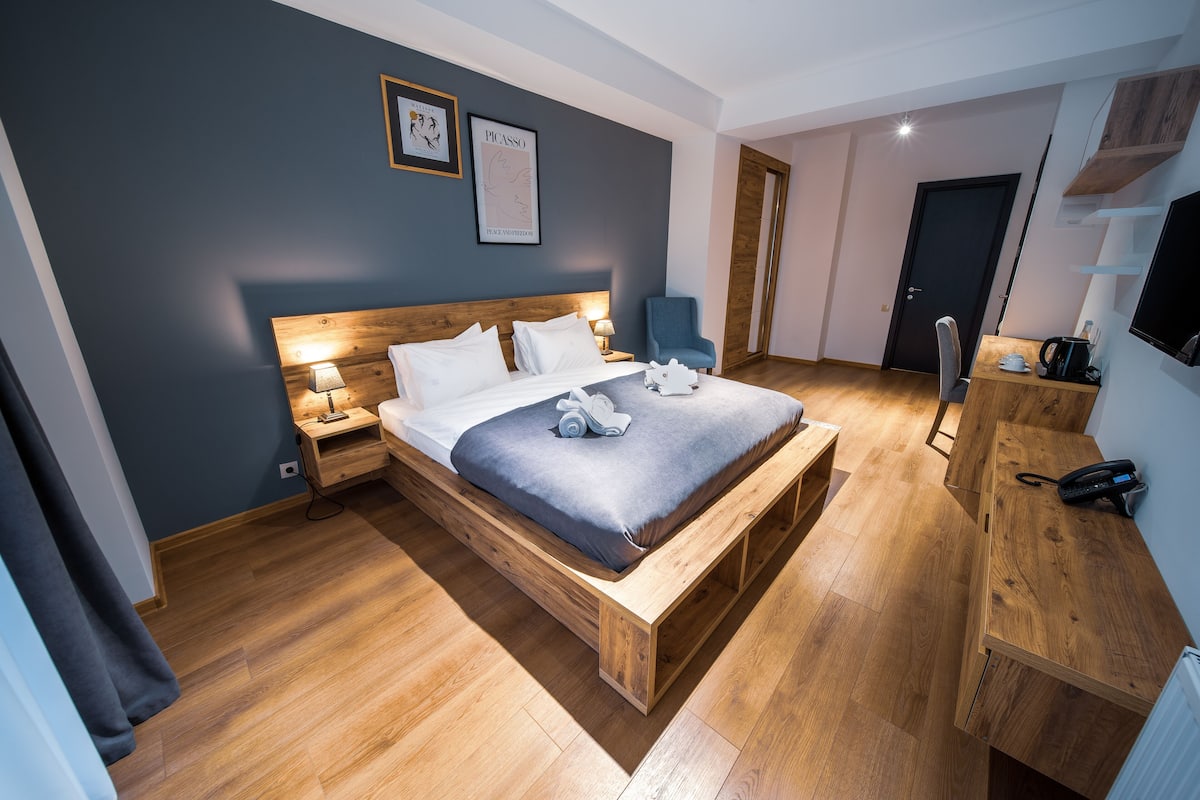 A modern bedroom with a wooden bed, a desk, a chair, and a television.