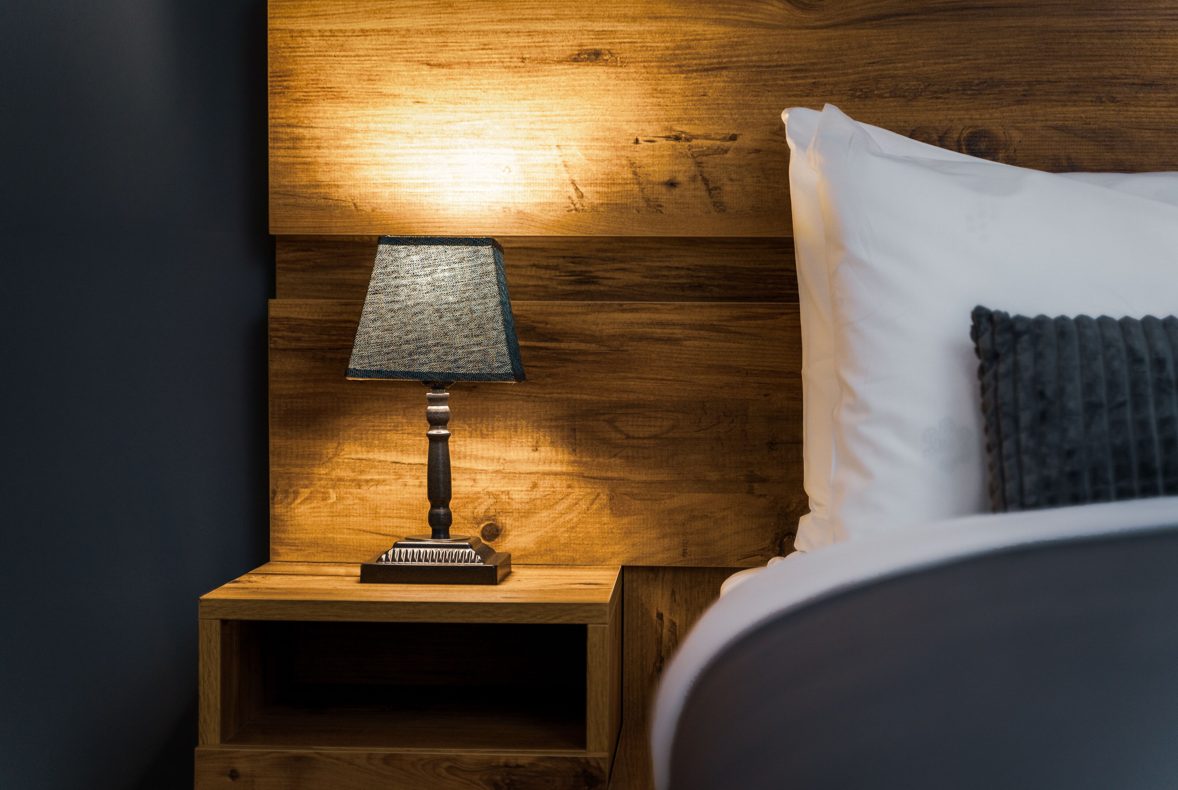 Een houten nachtkastje met een lamp en een wit kussen.