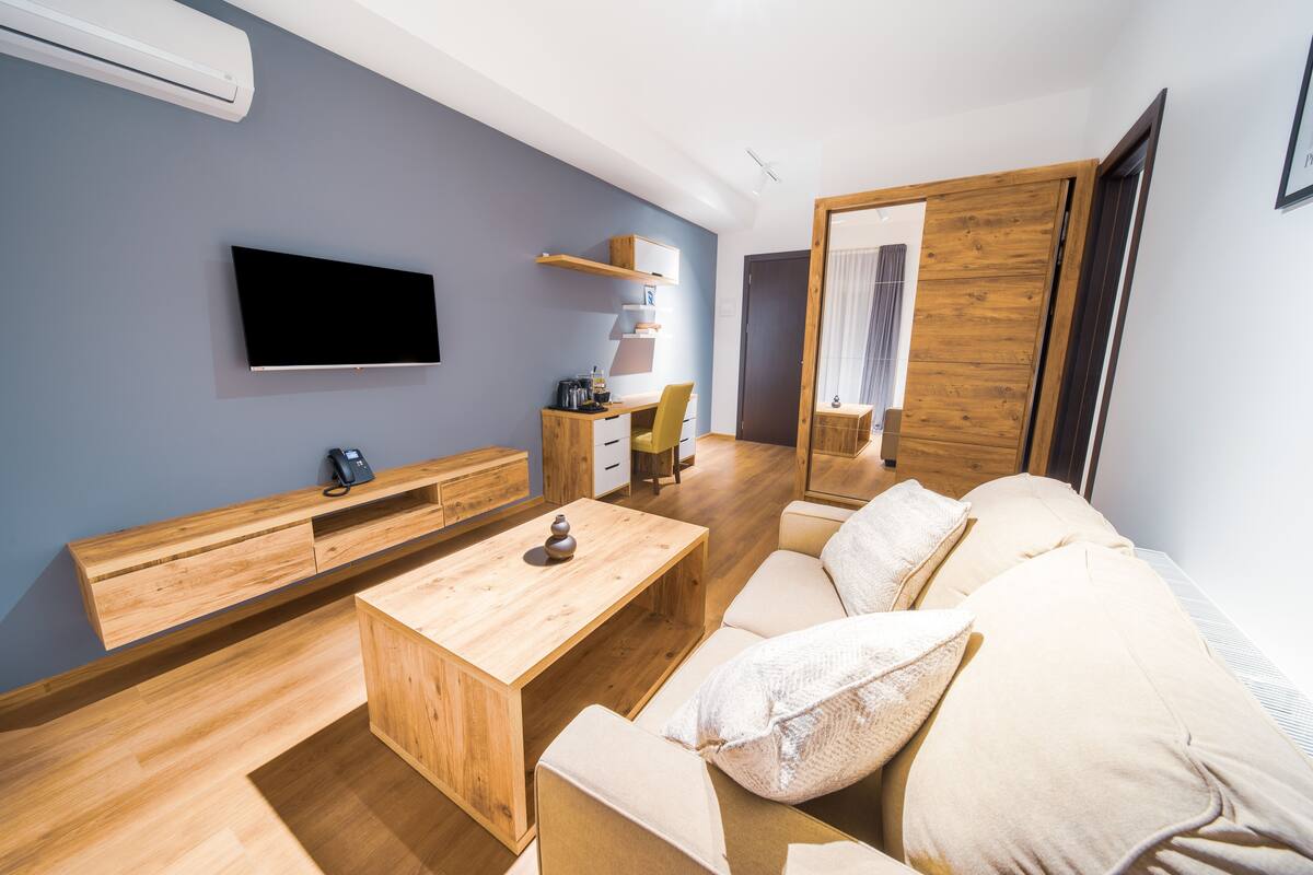 A modern living room with a flat-screen TV, wooden furniture, a sofa, and a wooden cabinet.