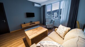 A modern living room with a sofa, a coffee table, a TV, and a window with a city view. - Reed Hotel Tbilisi (Tbilisi)